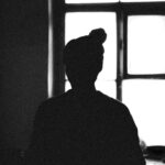 Monochrome silhouette of a person standing by a window, creating a dramatic mood.